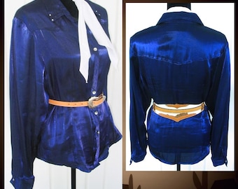 May include: A long-sleeved, royal blue button-down shirt with a subtle sheen, featuring a pointed collar, a white neck tie, and a tan leather belt with a metallic buckle. The shirt is displayed from both the front and back views on a mannequin.