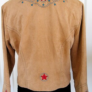 May include: Tan suede jacket with embroidered red stars and blue accents. Features a stand-up collar and long sleeves. The back has a large star design and the sleeves have smaller star details. A western-themed jacket.