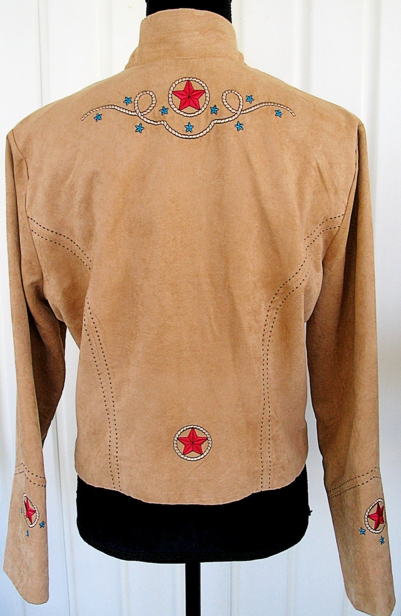 May include: Tan suede jacket with embroidered red stars and blue accents. Features a stand-up collar and long sleeves. The back has a large star design and the sleeves have smaller star details. A western-themed jacket.