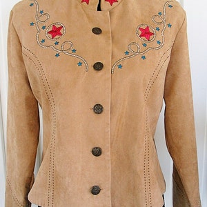 May include: Tan suede jacket with a mandarin collar and decorative stitching. Features embroidered red stars and turquoise accents with rope detailing. The jacket has four decorative buttons.