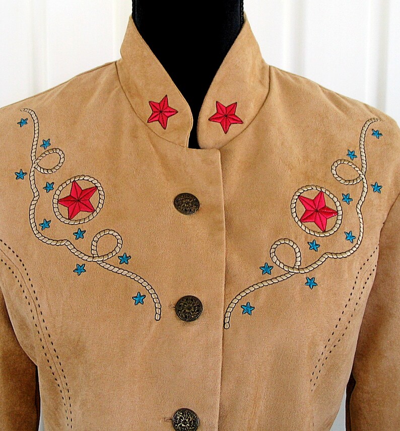 May include: A tan suede jacket with a mandarin collar and three decorative buttons. The jacket features embroidered red stars, blue stars, and rope detailing. The jacket has a western theme.