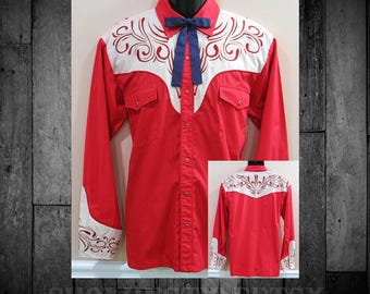 May include: A long-sleeve red shirt featuring a white yoke with red scrollwork embroidery, a dark blue neck tie, a button-down front, and two chest pockets. The shirt is displayed from the front, with an inset showing the back view.