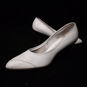 May include: A pair of white leather heeled shoes with a pointed toe. The shoes have a small heel and a simple design.