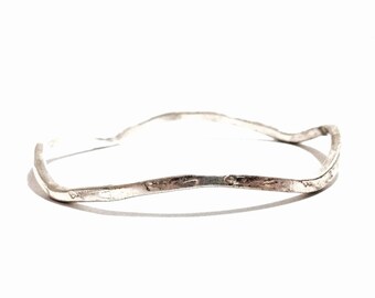 May include: A silver wavy bangle bracelet with a hammered finish.