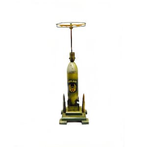 May include: A green and yellow metal model of a rocket with a black base and three smaller rockets on the base. The rocket has a black and yellow emblem on the side.