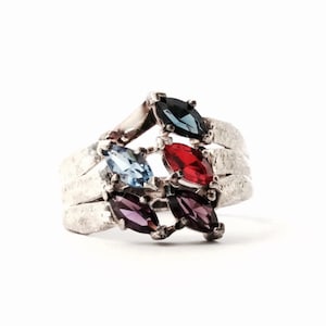 May include: A silver ring with five marquise-shaped gemstones. The gemstones are red, blue, purple, and black.