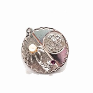 May include: Silver charm with a pearl, a red stone, and a silver coin with the words "Isle of Man" engraved on it.