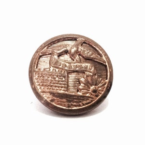 May include: A gold-toned metal button with a raised design of a bird perched on a branch with a flower below. The button has a smooth, shiny surface.