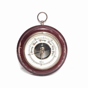 May include: A vintage wooden barometer with a round face and a silver needle. The face is marked with "Change", "Fair", and "Rain" and has a scale from 27 to 32.