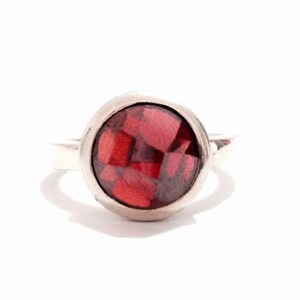 May include: A silver ring with a red gemstone set in a bezel setting.