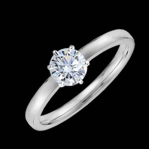 Puede incluir: Un anillo de compromiso solitario simple con un solo diamante redondo brillante engastado en una configuración de cuatro garras. La banda es un diseño clásico, liso y pulido.