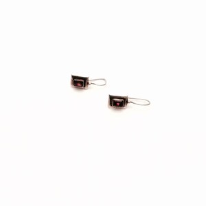 May include: A pair of silver earrings with small red gemstone accents. The earrings have a simple, rectangular design.