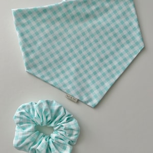 Puede incluir: Un conjunto de scrunchie y bandana con estampado de cuadros vichy azul claro y blanco. El bandana tiene una etiqueta blanca con el texto "Do & Co" en ella.