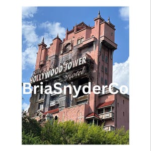 May include: A pink building with a sign that reads "The Hollywood Tower Hotel". The building is tall and has many windows. There are trees in the foreground.
