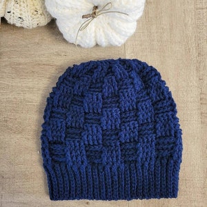 May include: A navy blue crocheted beanie hat with a textured woven pattern. The hat is made with a thick yarn and has a folded brim.