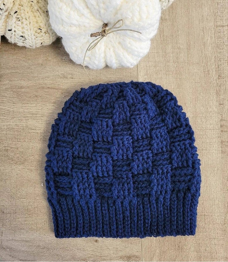 May include: A navy blue crocheted beanie hat with a textured woven pattern. The hat is made with a thick yarn and has a folded brim.