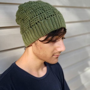 May include: A green crocheted beanie with a textured stitch pattern. The beanie is worn by a person with dark hair.