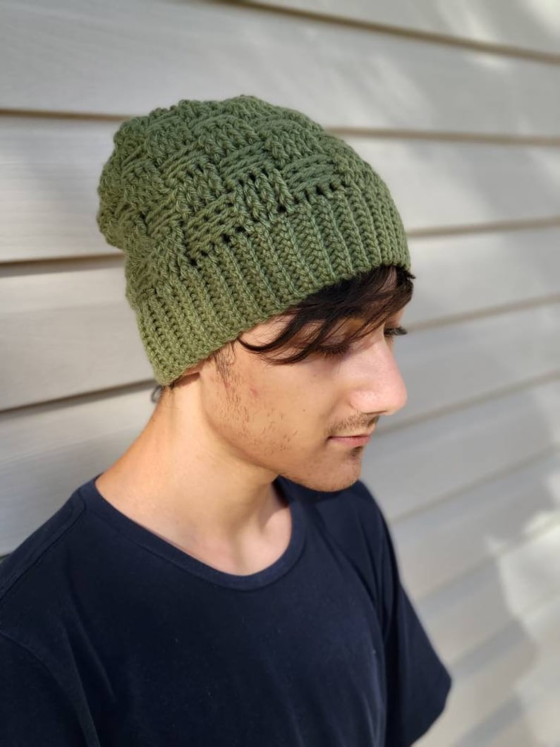 May include: A green crocheted beanie with a textured stitch pattern. The beanie is worn by a person with dark hair.