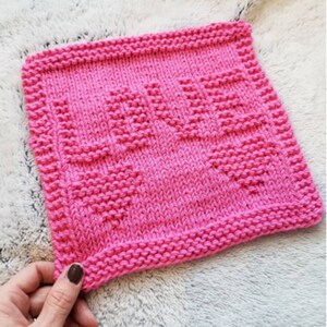 May include: Pink knitted dishcloth with the word "LOVE" in a heart shape pattern. Knitting pattern.