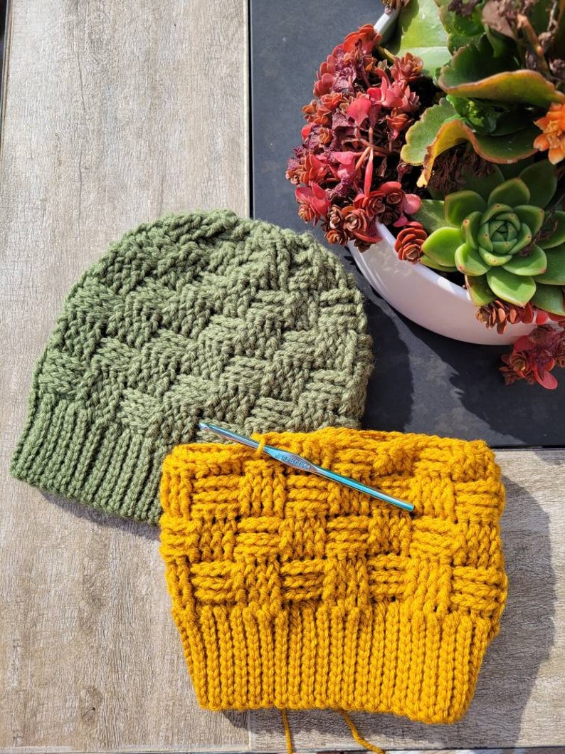 May include: Two crocheted hats, one green and one yellow, with a crochet hook laying across the yellow hat.