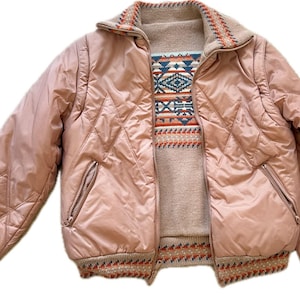 May include: A vintage pink quilted jacket with a zip closure and a patterned sweater underneath. The jacket has a diamond pattern, ribbed cuffs, and a collar with a patterned trim. The sweater features a geometric design.