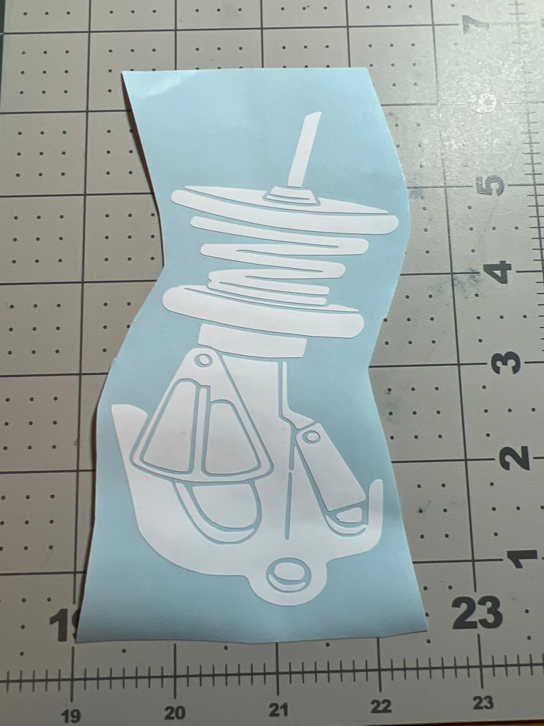 May include: White vinyl sticker of a car suspension coil spring with a shock absorber. The sticker is on a blue background.