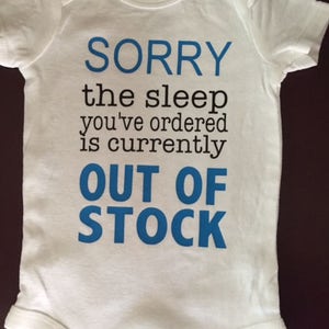 May include: White baby onesie with the text "SORRY the sleep you've ordered is currently OUT OF STOCK" in blue and black lettering. The onesie has short sleeves and a round neckline.