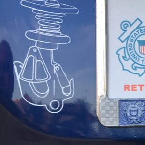May include: A white sticker on a blue car with a drawing of a boat anchor and a spring. The sticker is next to a silver number plate with the United States Coast Guard emblem and the text "RET"