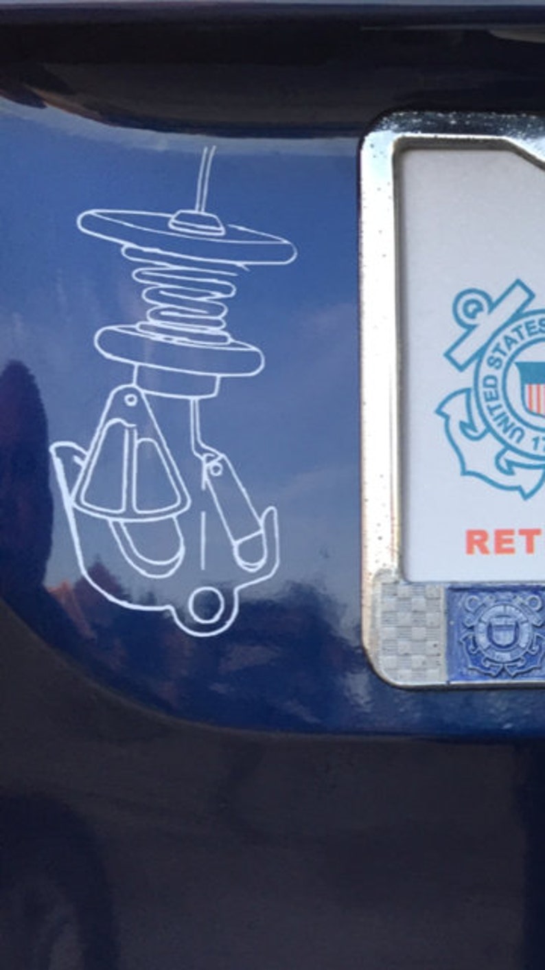 May include: A white sticker on a blue car with a drawing of a boat anchor and a spring. The sticker is next to a silver number plate with the United States Coast Guard emblem and the text "RET"