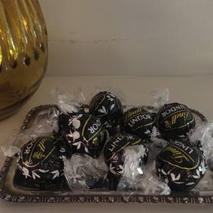 May include: A silver tray containing a selection of Lindor chocolate truffles. The truffles are wrapped in silver foil and have a dark chocolate exterior. The tray has a scalloped edge.
