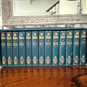 May include: A set of twelve teal-colored Shakespeare books in a matching case. The books are arranged in a row, with gold lettering and decorative elements on the spines. The books are labeled with Roman numerals.