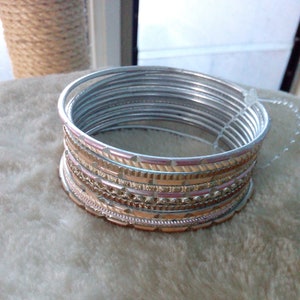 May include: A set of silver and gold bangles with intricate designs. The bangles are stacked on top of each other and have a shiny finish.