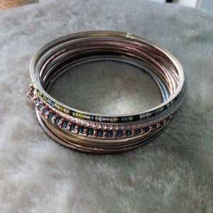 May include: A set of stacked bangles with a beaded design in shades of gold, silver, and blue.