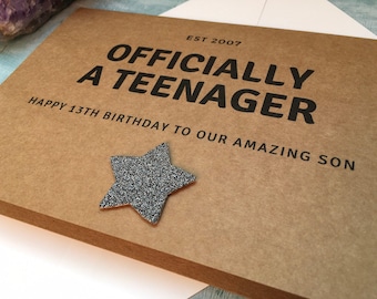 May include: A brown card with the text "OFFICIALLY A TEENAGER" and "HAPPY 13TH BIRTHDAY TO OUR AMAZING SON." A silver glitter star is affixed to the card. The text "EST 2007" is above the main text.