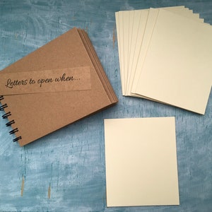 May include: A brown kraft paper journal with a spiral binding and a tag that says "Letters to open when..."  The journal is accompanied by a stack of blank ivory cards.