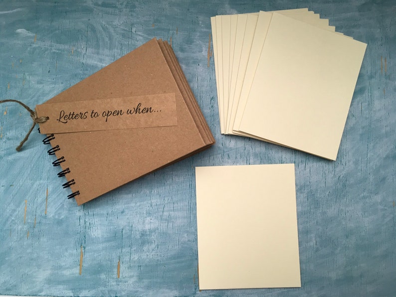 May include: A brown kraft paper journal with a spiral binding and a tag that says "Letters to open when..."  The journal is accompanied by a stack of blank ivory cards.
