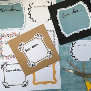 May include: Assorted paper cutouts with the text "Open when..." in various decorative frames. Includes a kraft paper card, a black card, and several white cards with different border designs. A pair of scissors with yellow handles is also visible.