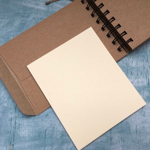 May include: A brown paper notebook with a blank white page open. The notebook is bound with a black wire coil.