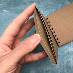 May include: A brown spiral bound notebook with a blank cover. The notebook is open and the pages are visible.