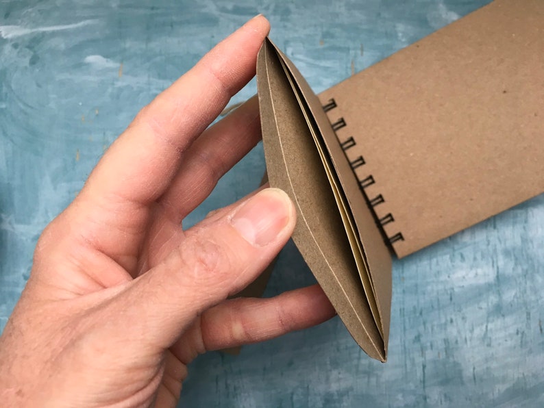 May include: A brown spiral bound notebook with a blank cover. The notebook is open and the pages are visible.