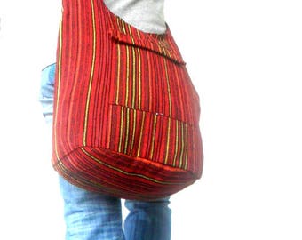 Può includere: Una borsa a tracolla in tessuto a righe rosse, gialle e nere con una tasca a lembo. La borsa è indossata da una persona che indossa jeans blu.