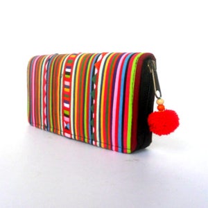 Puede incluir: Una cartera con cremallera de rayas coloridas con un abalorio de pomp&oacute;n rojo. La cartera est&aacute; hecha de tela y tiene una cremallera negra.