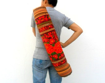 Puede incluir: Un portador de esterilla de yoga floral rojo y naranja con una correa larga. El portador está hecho de tela y tiene un diseño tradicional.