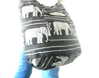 May include: A black and white patterned tote bag with a design of elephants. The bag is worn over the shoulder of a person wearing blue jeans.