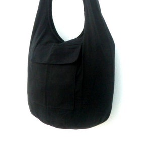 Pode incluir: Uma bolsa tote de lona preta com um bolso grande na frente. A bolsa tem uma al&ccedil;a longa para carregar no ombro.