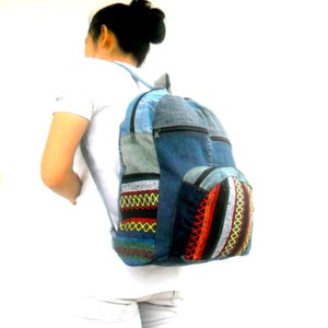 May include: A blue denim backpack with colorful embroidered details. The backpack has a large main compartment and a smaller front pocket. The backpack is made from recycled materials.