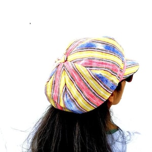 May include: A striped yellow, pink, blue, and white fabric newsboy cap with a curved brim.