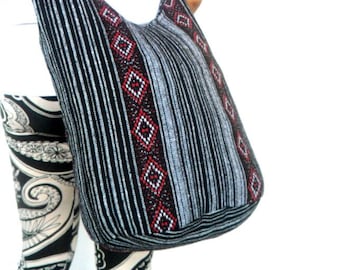 May include: A black and white striped tote bag with red and white geometric patterns. The bag has a long strap and is made of a woven fabric.