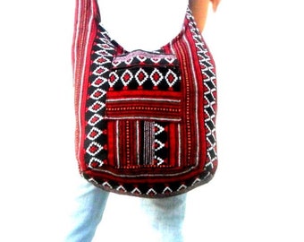 Può includere: Una borsa a tracolla con un motivo geometrico rosso, nero e bianco. La borsa ha una lunga tracolla e una tasca frontale con cerniera. La borsa è realizzata in tessuto intrecciato.