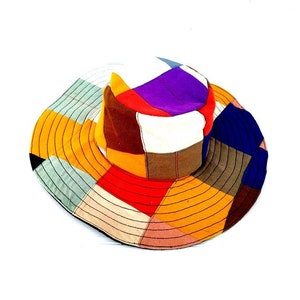 Puede incluir: Un sombrero de sol de patchwork colorido con un ala ancha. El sombrero está hecho de telas de diferentes colores, incluyendo rojo, naranja, amarillo, verde, azul, morado y marrón.